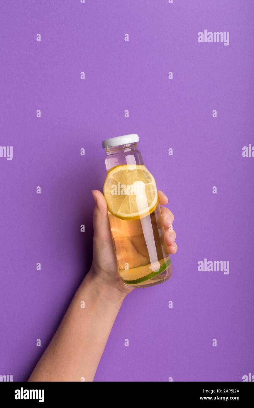 Frau, die Zitronendetox in einer Glasflasche auf violett präsentiert Stockfoto