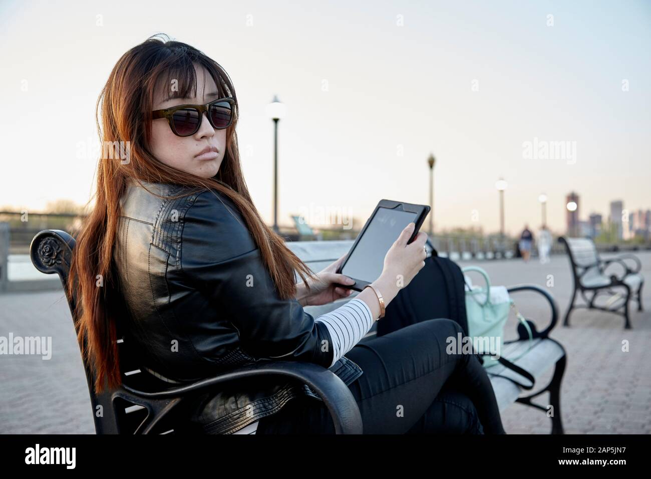 Asiatische Frau sitzt auf der Bank mit Tablet und trägt Sonnenbrille Stockfoto
