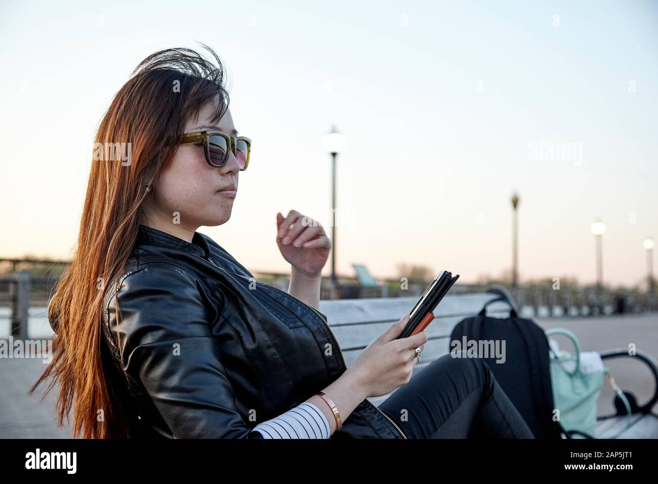 Asiatische Frau sitzt auf der Bank mit Tablet und trägt Sonnenbrille Stockfoto