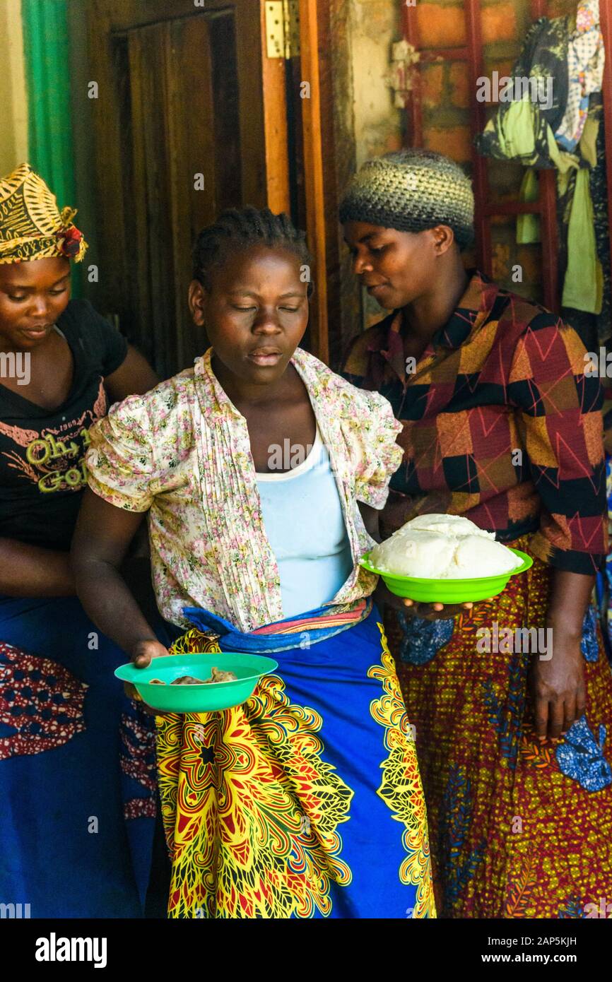 Malawische Frauen tragen traditionelle Kleidung und eine frisch zubereitete Mahlzeit Von Nsima und Huhn in Plastikschüsseln Stockfoto