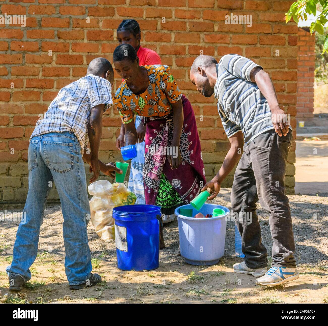 Malawische Frauen servieren Männern Tee aus einem Plastikeimer In einem Dorf Stockfoto