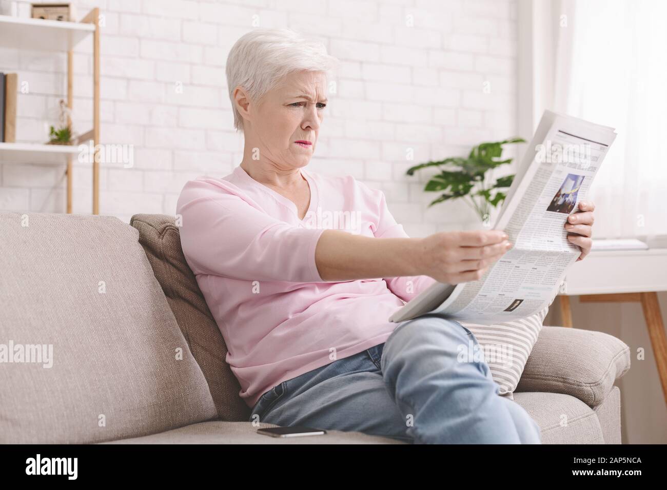 Die Seniorin quietscht und hält die Zeitung fern der Augen Stockfoto