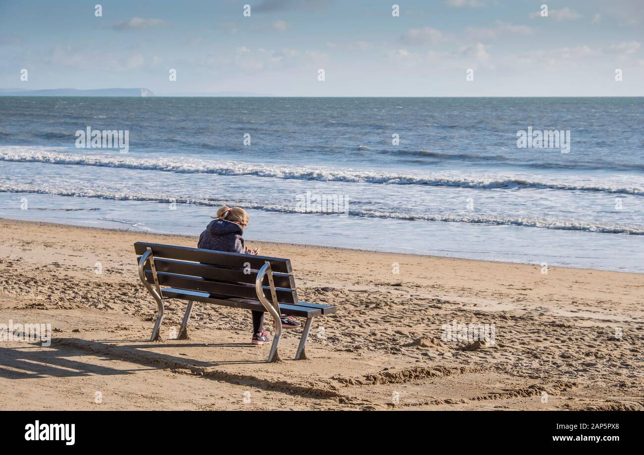 Bournemouth Beach mit einer Person, die im Winter allein auf der Promenade sitzt und dabei ein Handy benutzt. Stockfoto
