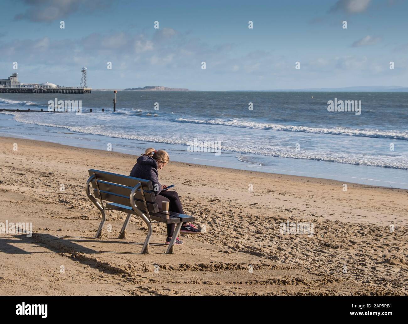 Bournemouth Beach mit einer Person, die im Winter allein auf der Promenade sitzt und dabei ein Handy benutzt. Stockfoto