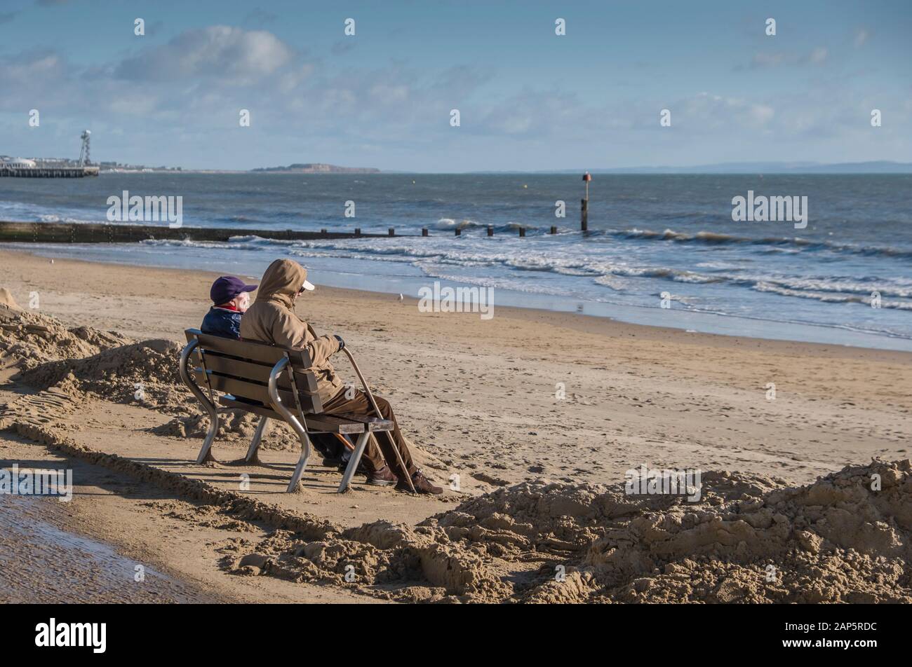 Bournemouth Beach mit einem reiferen Paar, das im Winter allein auf der Promenade sitzt. Stockfoto