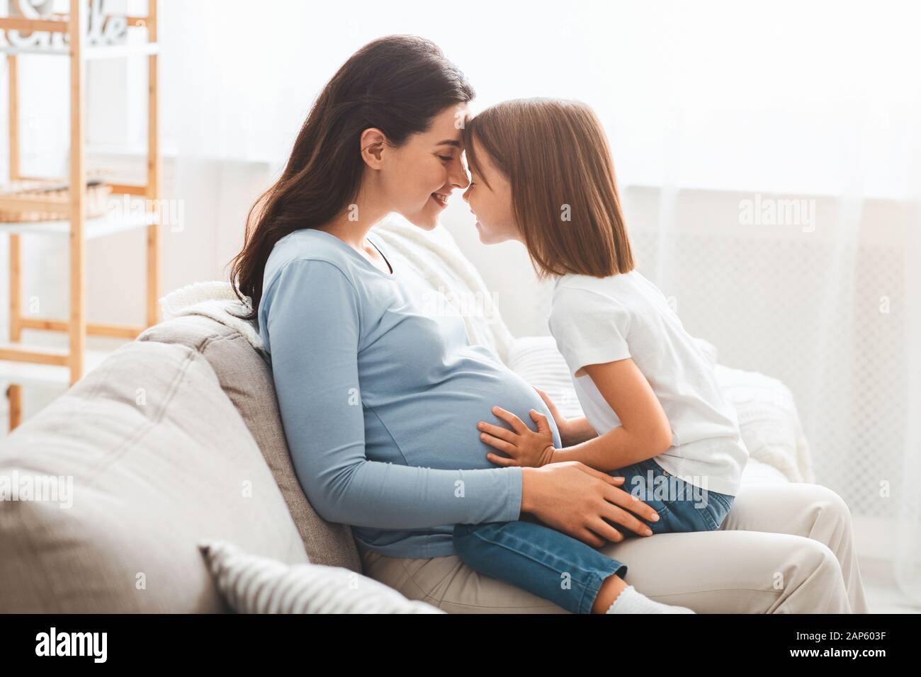 Junge schwangere Frau, die sich mit ihrer kleinen Tochter verbüngert Stockfoto