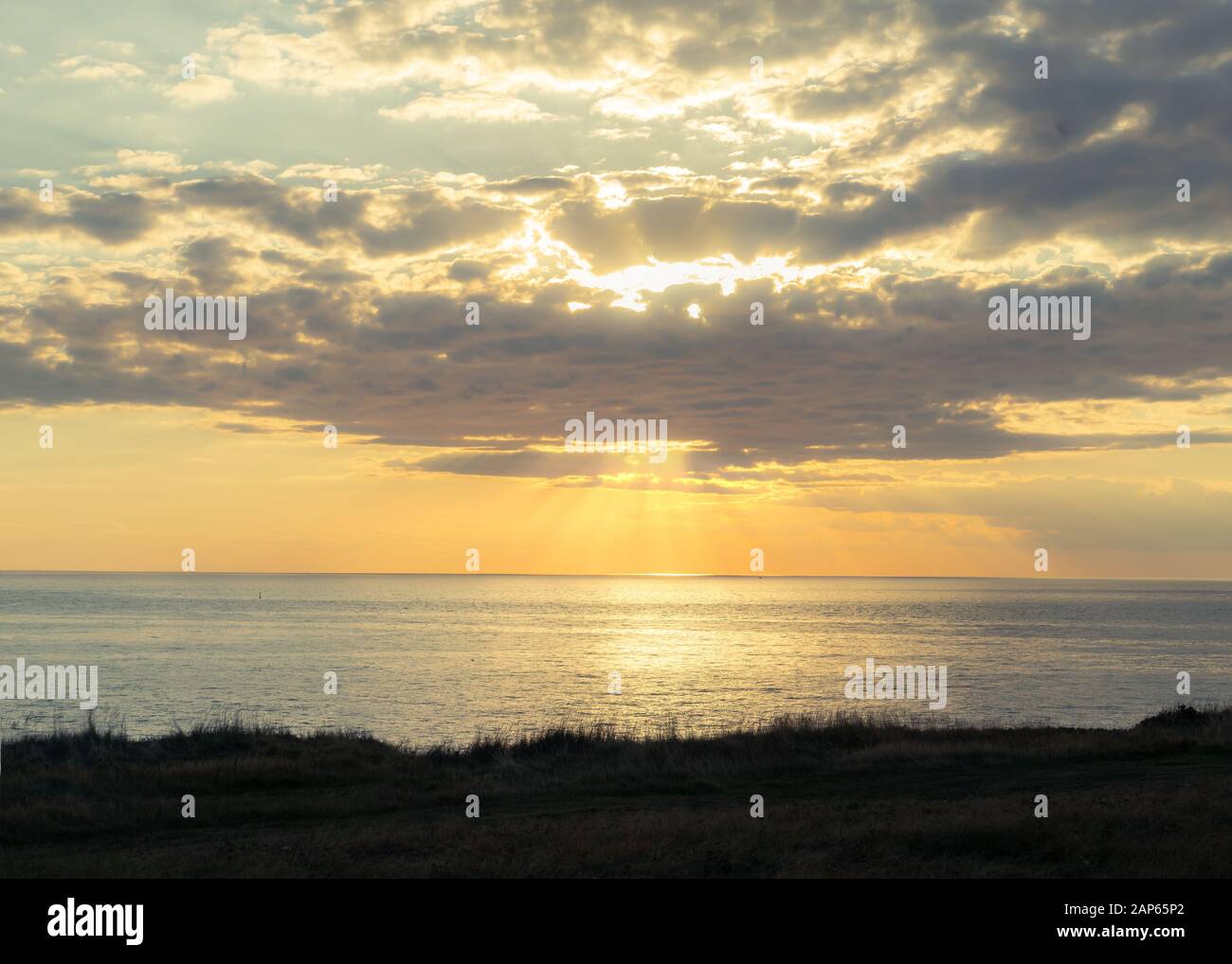 Wolken verdunkeln die Sonne bei Sonnenuntergang über einem Ozean Vista. Stockfoto