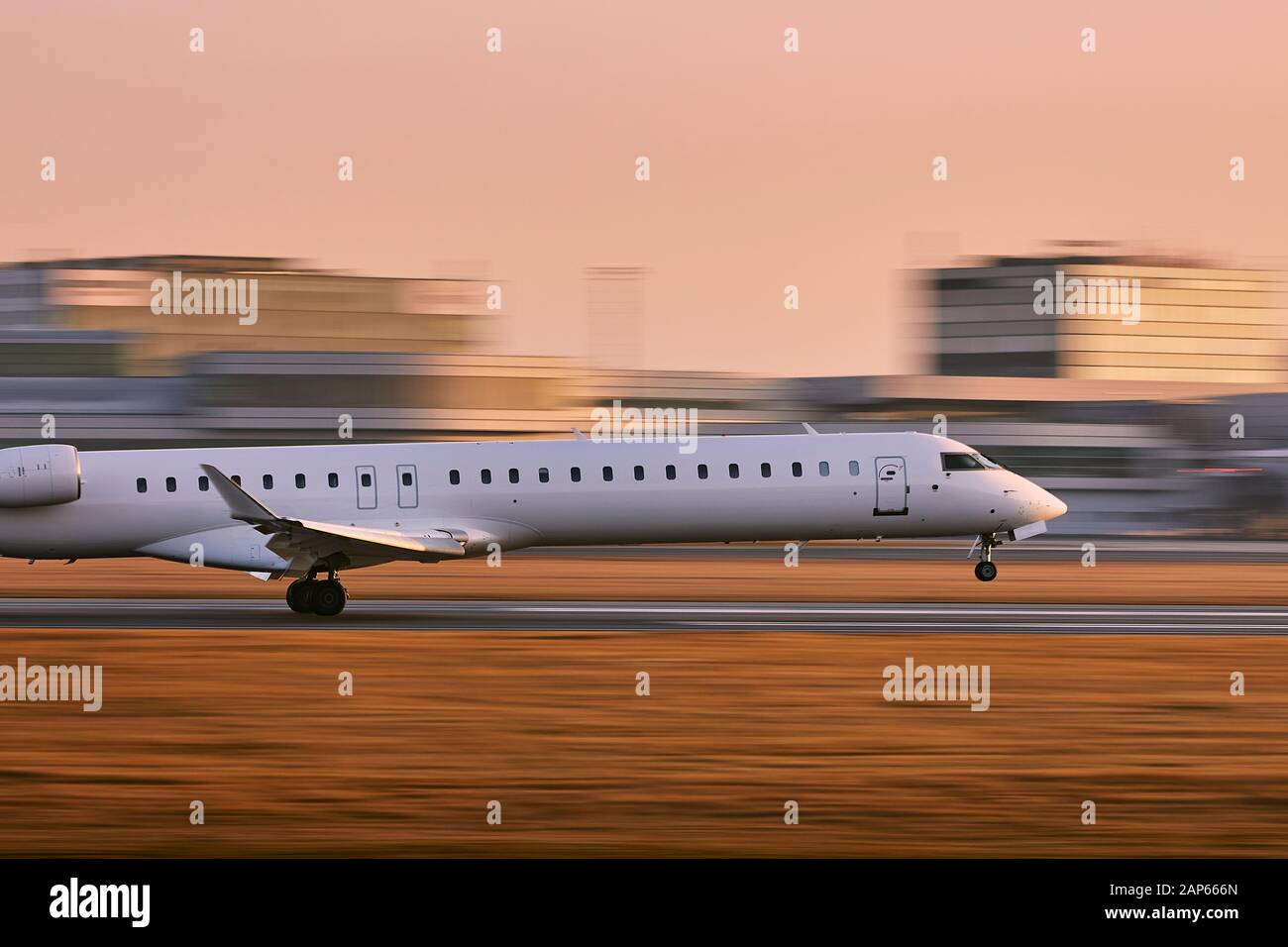 Verkehr am Flughafen. Flugzeug Landung auf Piste gegen Terminal Gebäude im Golden Sunset (verschwommene Bewegung). Stockfoto