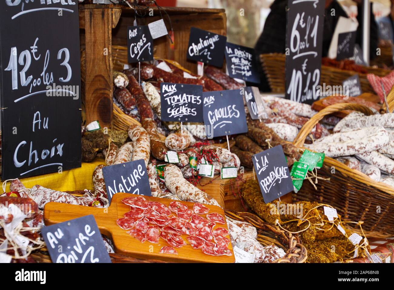 Verschiedene Arten französischer Salami-Provenzale, die in Korbkörben mit handschriftlichen Kreideplatten auf dem Bauernmarkt präsentiert werden - St. Tropez, Frankreich Stockfoto