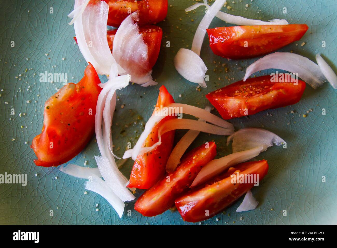 Hochwinkelige Draufsicht Nahaufnahme von frischen rohen roten Tomatenscheiben mit Zwiebeln, gewürzt mit Kräutersalz auf grünem Teller Stockfoto
