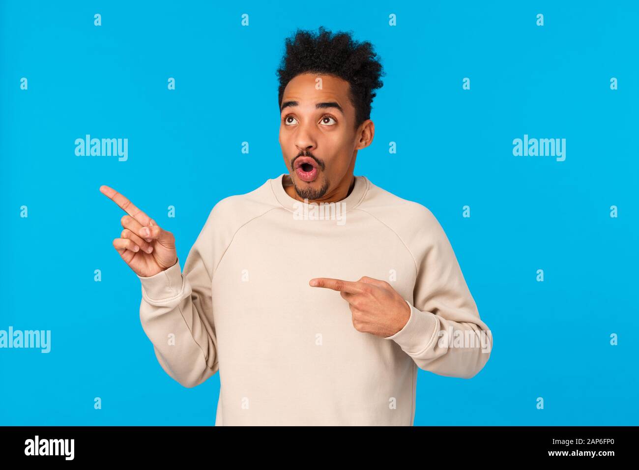 Sprachlos und beeindruckt, erschrocken attraktiver afroamerikanischer Freund, der genau das sieht, was er braucht, und die Rede vor blauem Hintergrund und offenem Mund verliert Stockfoto