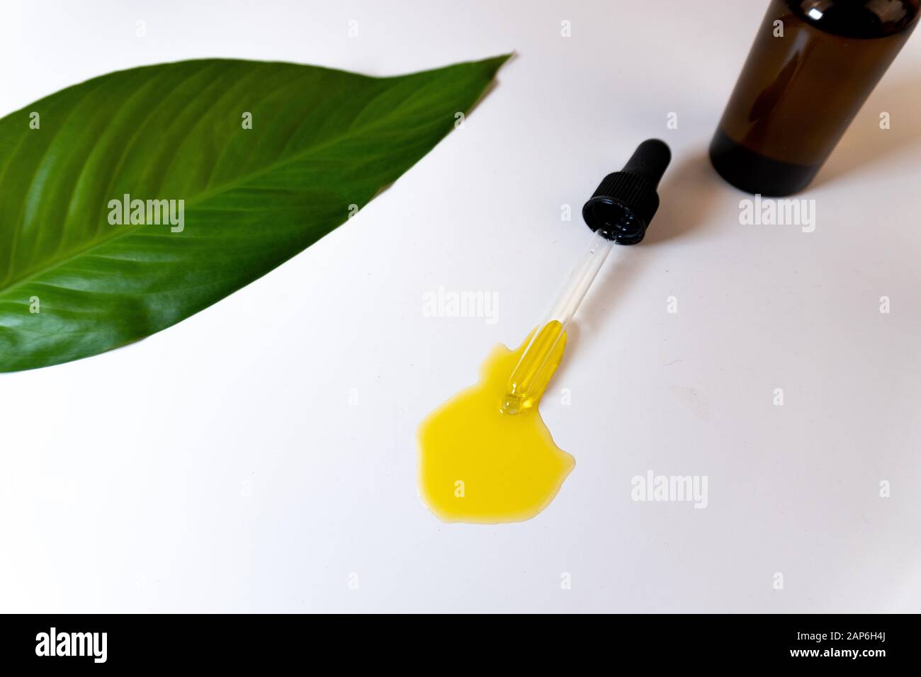 Draufsicht auf eine Flasche mit CBD-Öl oder anderem ätherischem Öl und einem grünen Blatt auf weißem Hintergrund Stockfoto