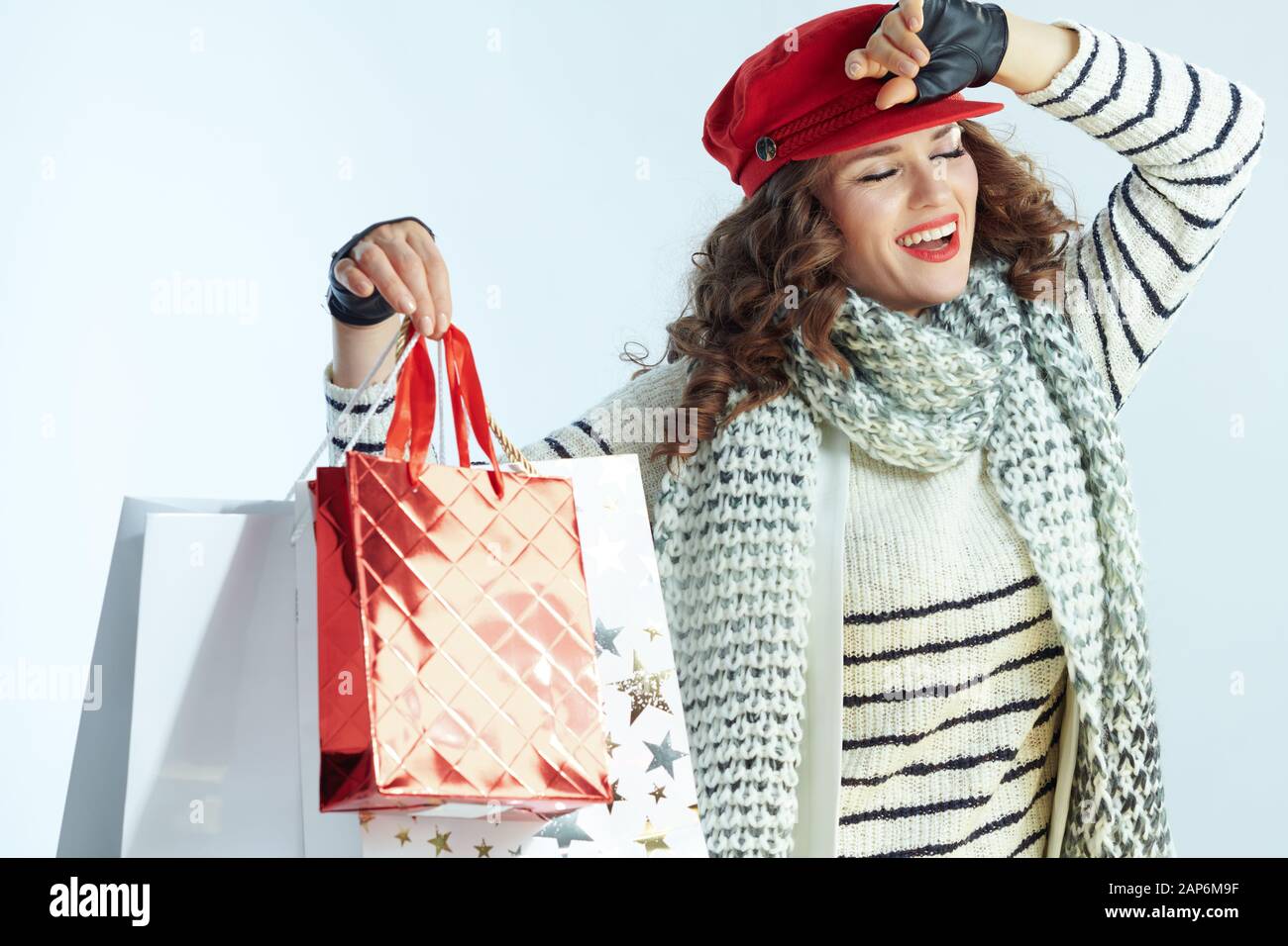 Glücklich, elegante Frau mit langen brünetten Haar in Pullover, Schal und Red Hat mit Tüten auf Winter hellblauen Hintergrund isoliert. Stockfoto