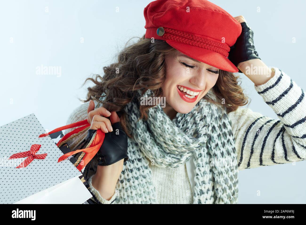 Lächelnd stilvolle Frau mit langen brünetten Haar in Pullover, Schal und Red Hat mit Tüten gegen Winter hellblau hinterlegt. Stockfoto