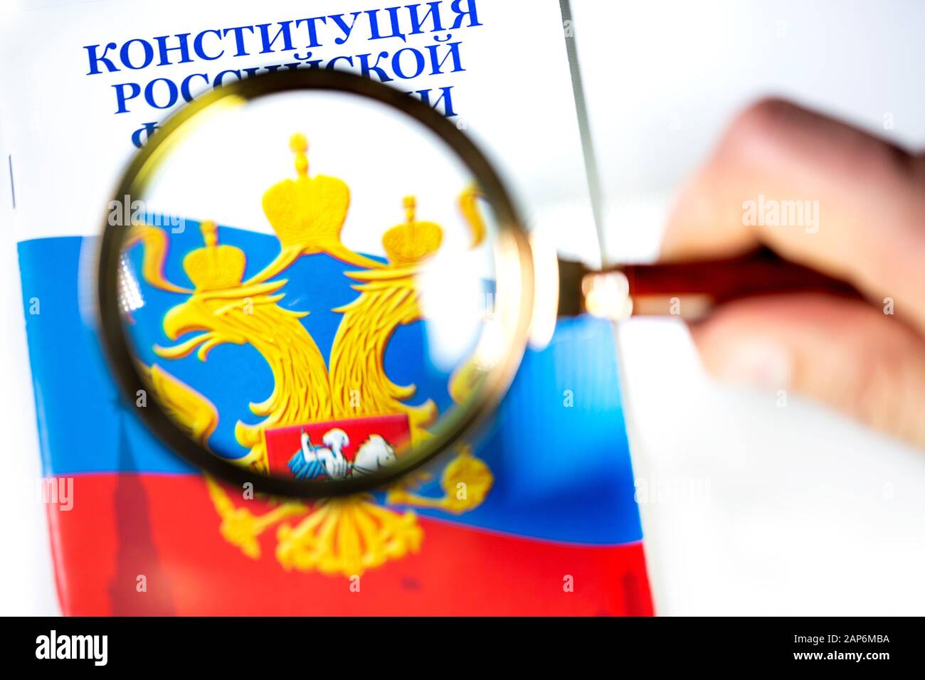 Ein Mann studiert Die Verfassung der Russischen Föderation unter einer Lupe auf weißem Hintergrund Stockfoto