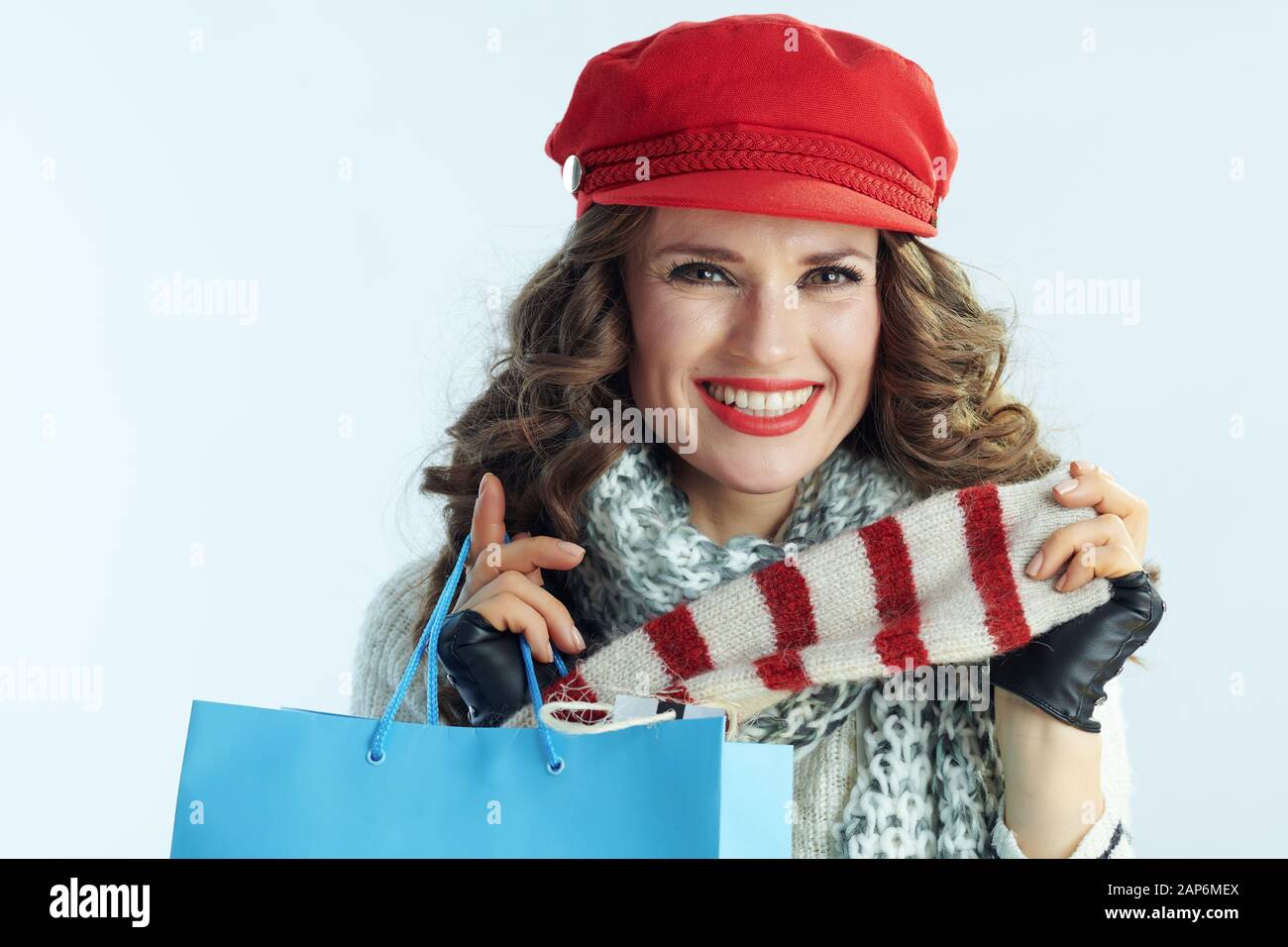 Portrait von Happy Elegant 40 Jahre alte Frau mit langen brünetten Haar in Pullover, Schal und Red Hat mit blau Einkaufstasche, Käufe gegen wi Stockfoto