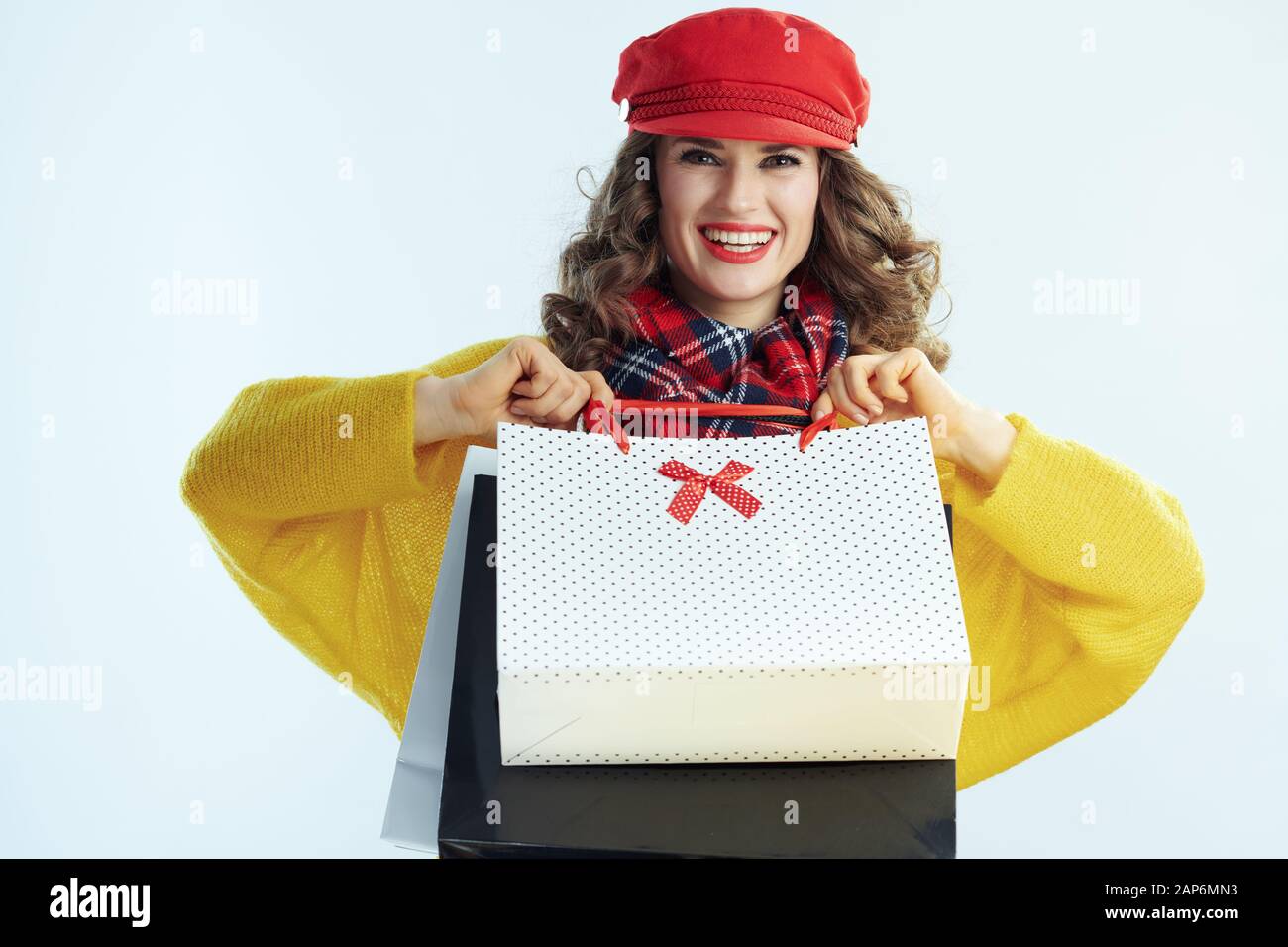 Happy Elegant 40 Jahre alte Frau mit langen brünetten Haar in Pullover, Schal und Red Hat mit Einkaufstaschen im Winter hellblauen Hintergrund isoliert. Stockfoto