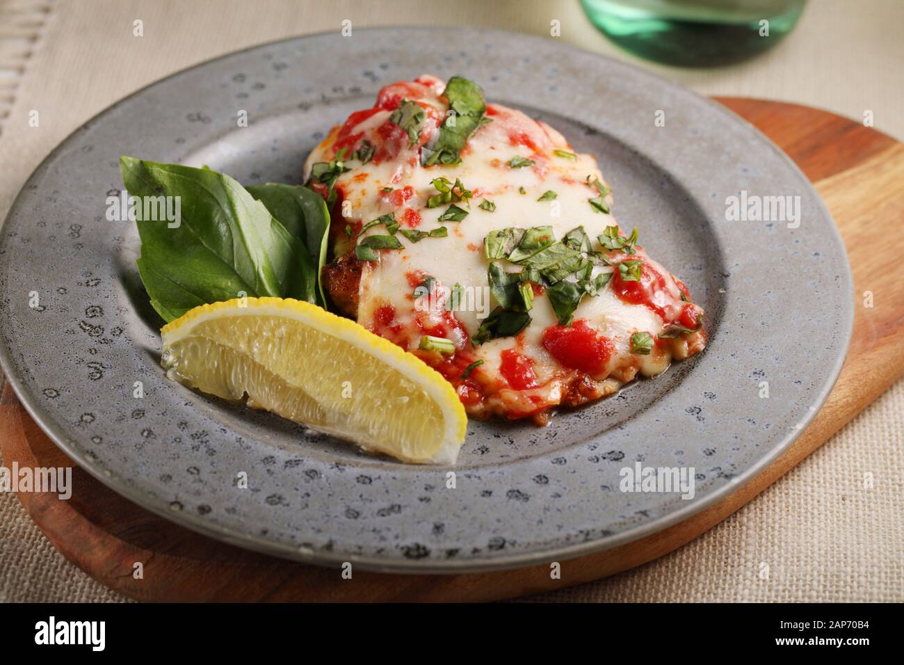 Hühnchen Parmigiana auf einem grauen Platte serviert mit Scheibe der Zitrone und Basilikum Blatt Stockfoto