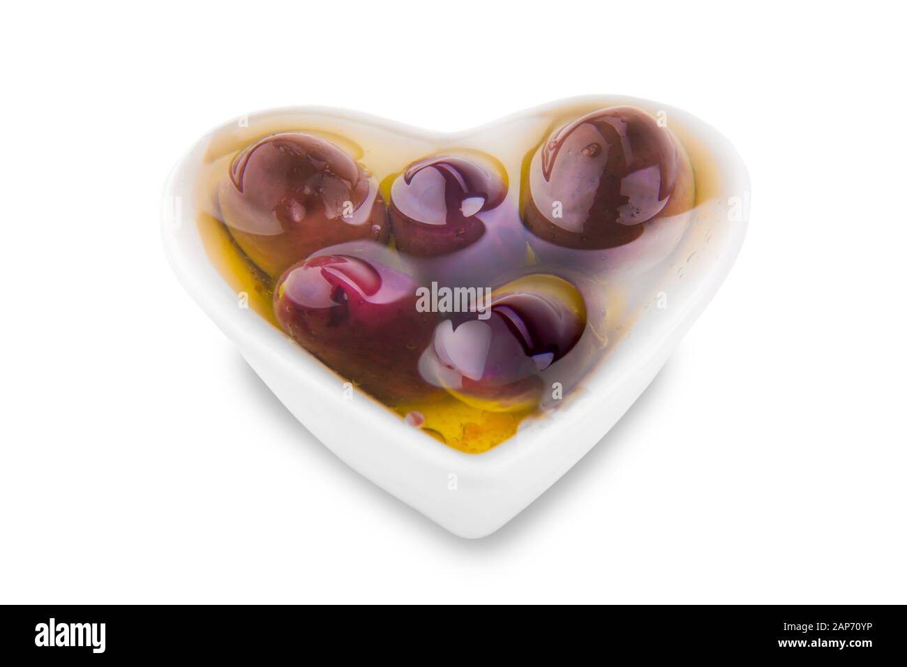Herzförmige Schüssel auf weißem Grund mit dunklen Oliven in Olivenöl Stockfoto