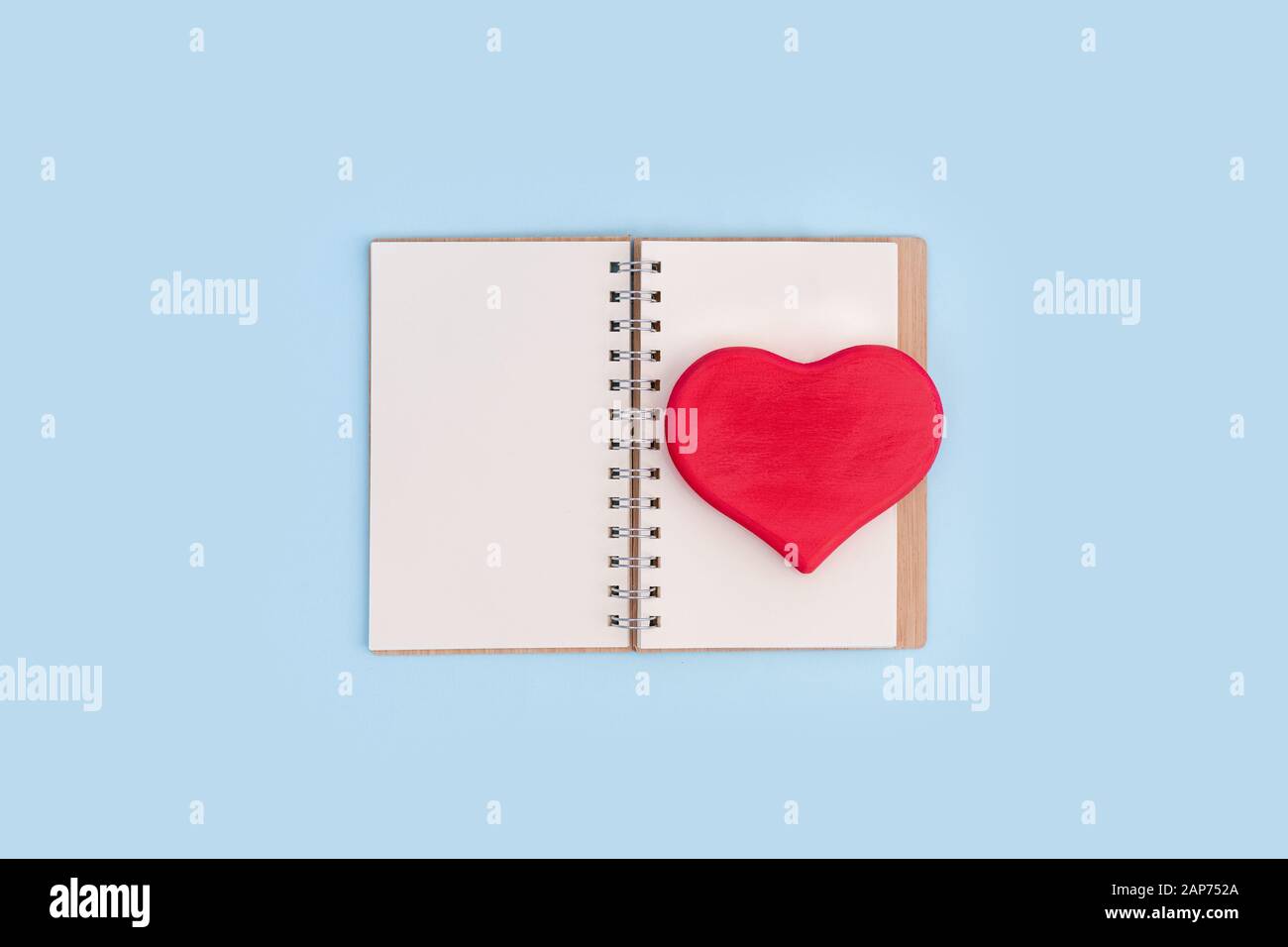 Rotes Holz-Liebesherz auf offenem Notizbuch auf blauem Hintergrund. Valentinstag Konzept, Kopierraum. Stockfoto