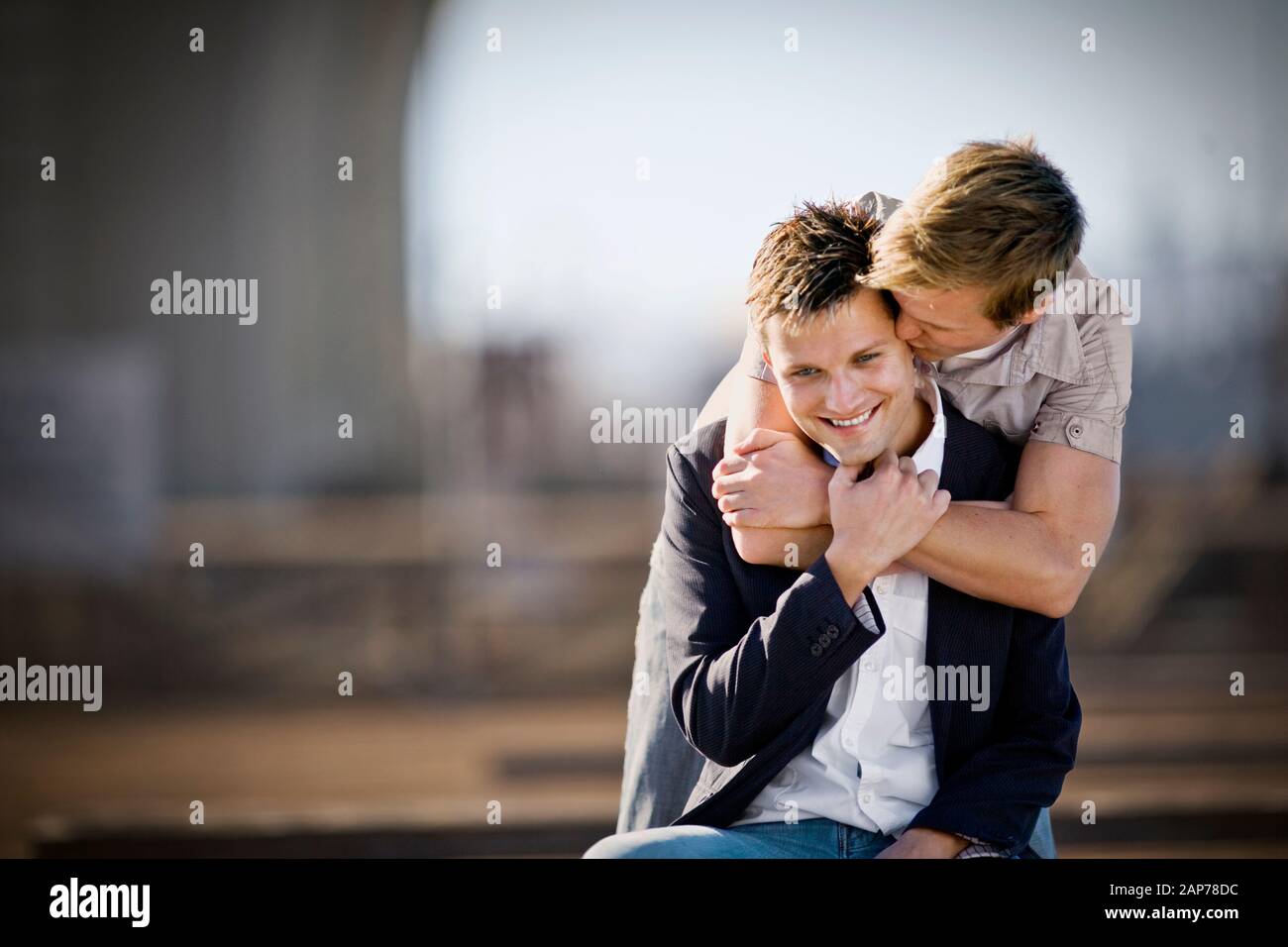 Männer mittlerer Erwachsener, der von seinem Partner umarmt und geküsst wird, während er draußen ist. Stockfoto