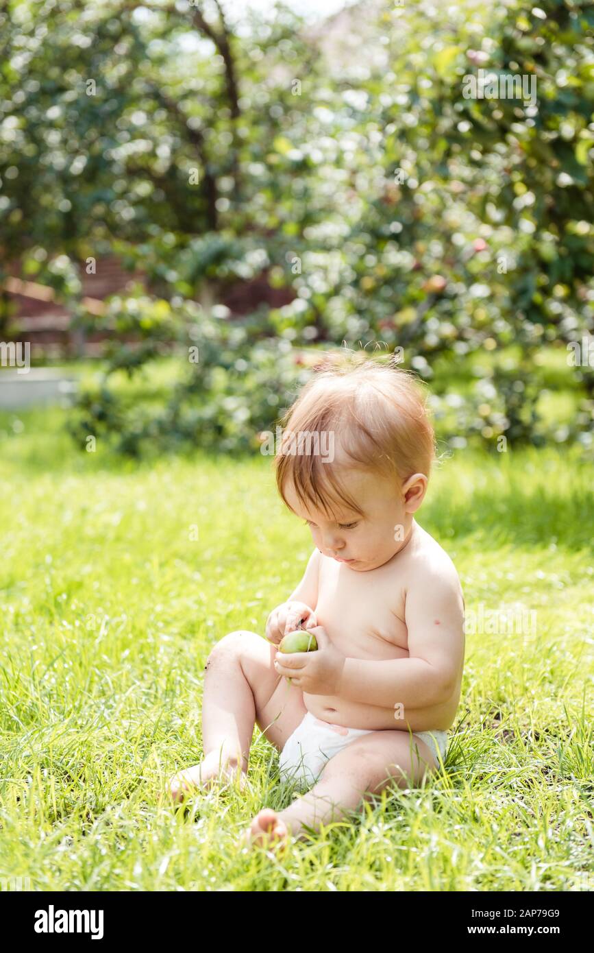 Kleiner Junge sitzt auf dem Gras und hält einen Apfel Stockfoto