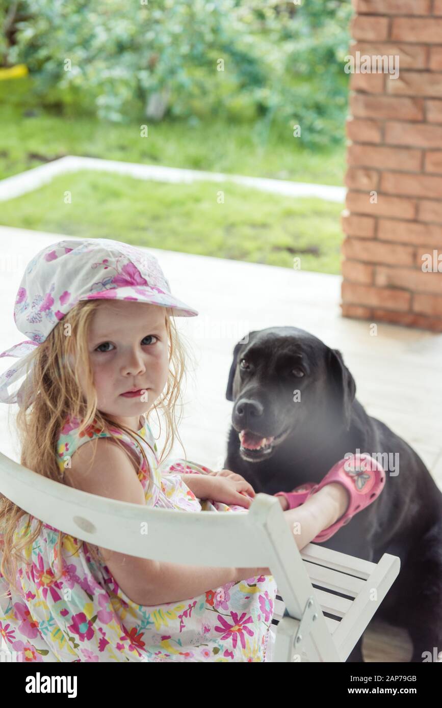 Mädchen sitzt im Hof mit einem großen schwarzen Hund Stockfoto
