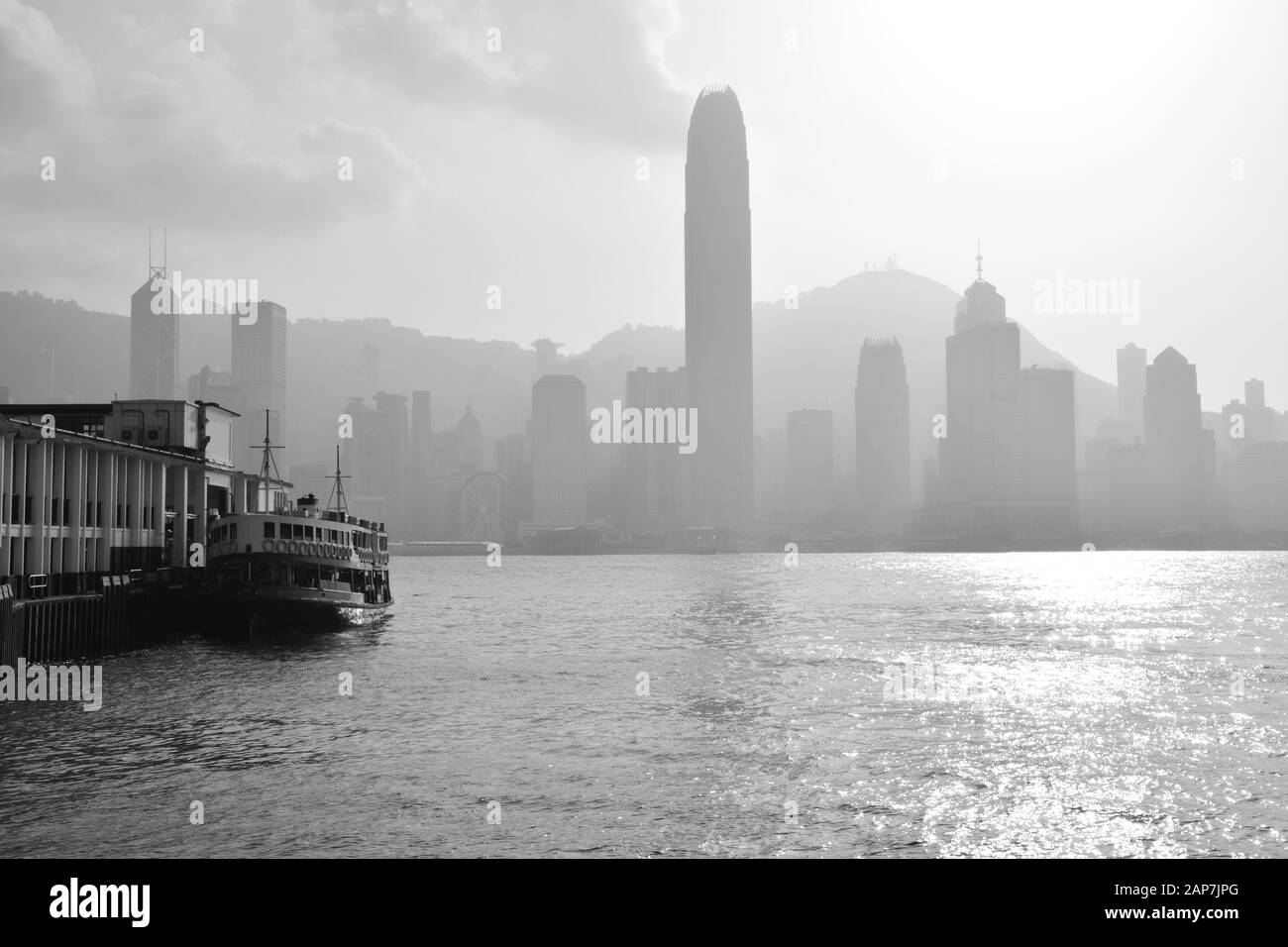 Schwarz-Weiß-Bild der Kreuzung der Star Ferry zwischen Central District und Kowloon Peninsula mit einem Smog, der über der Innenstadt von Hongkong hängt. Stockfoto