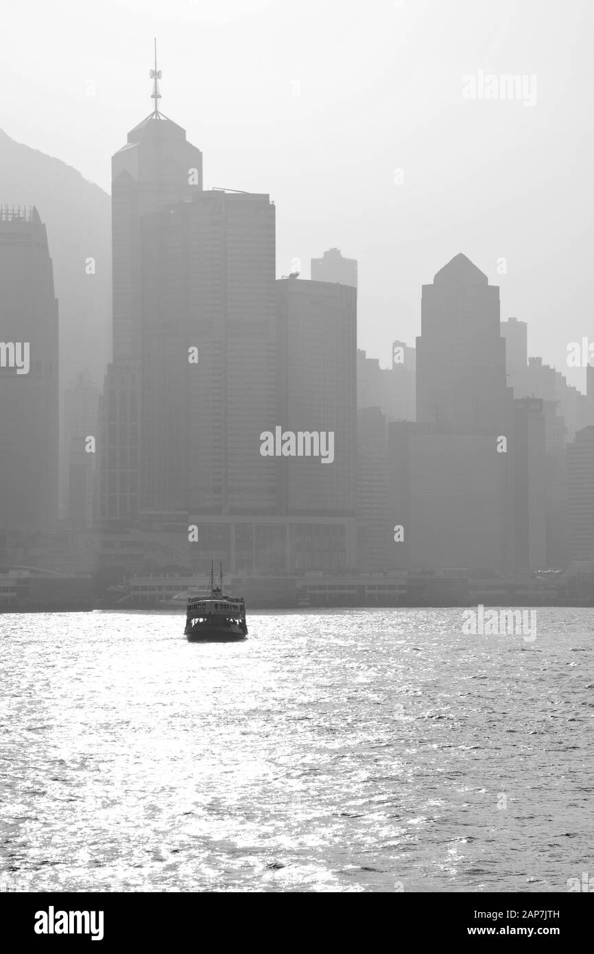 Schwarz-Weiß-Bild der Kreuzung der Star Ferry zwischen Central District und Kowloon Peninsula mit einem Smog, der über der Innenstadt von Hongkong hängt. Stockfoto