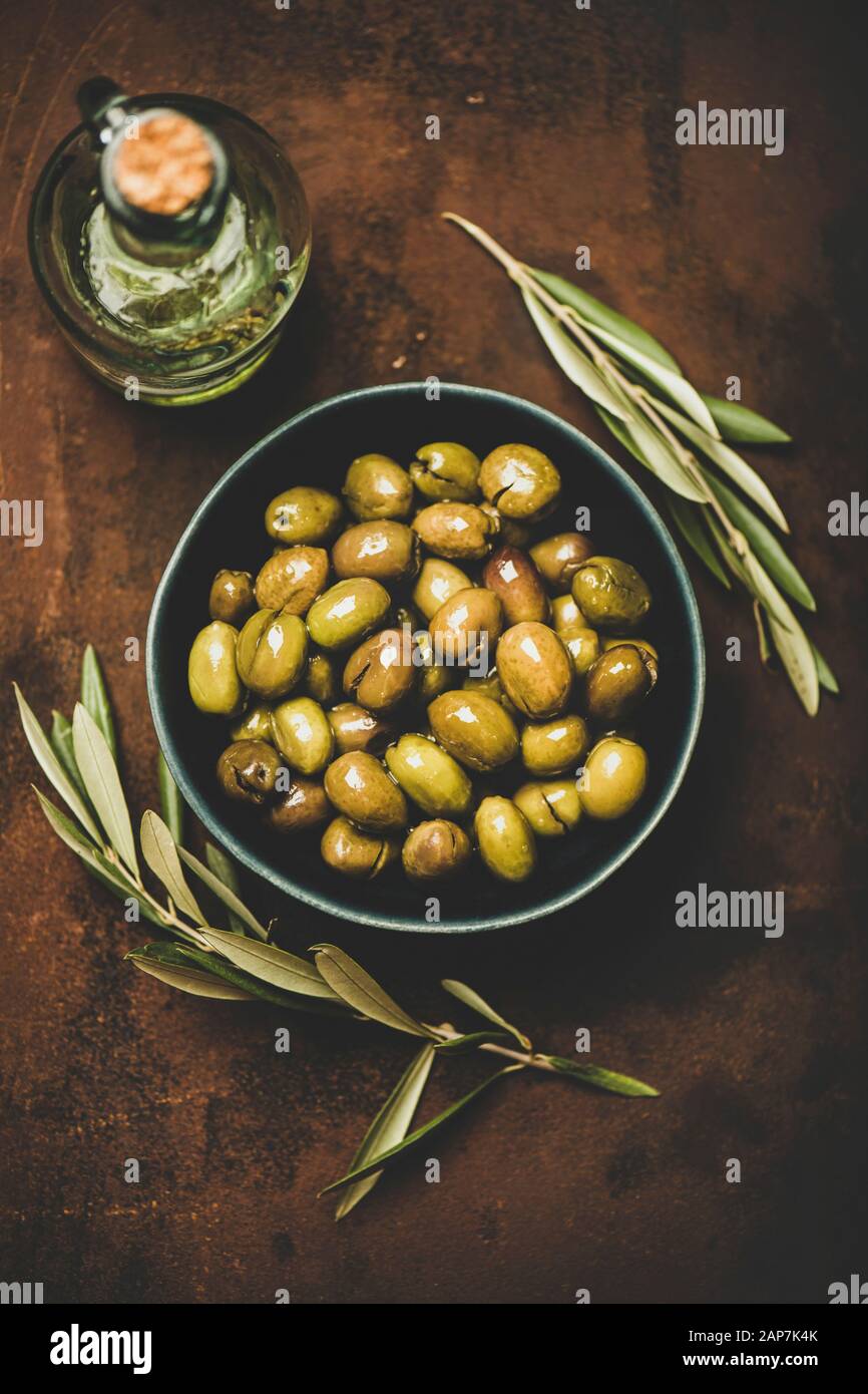 Flachbild-lay von frisch geerntete saisonale Eingelegte grüne mediterrane Oliven in Schale und Olivenöl in der Flasche über dunkle Rusty Hintergrund, Ansicht von oben. Gesund Stockfoto
