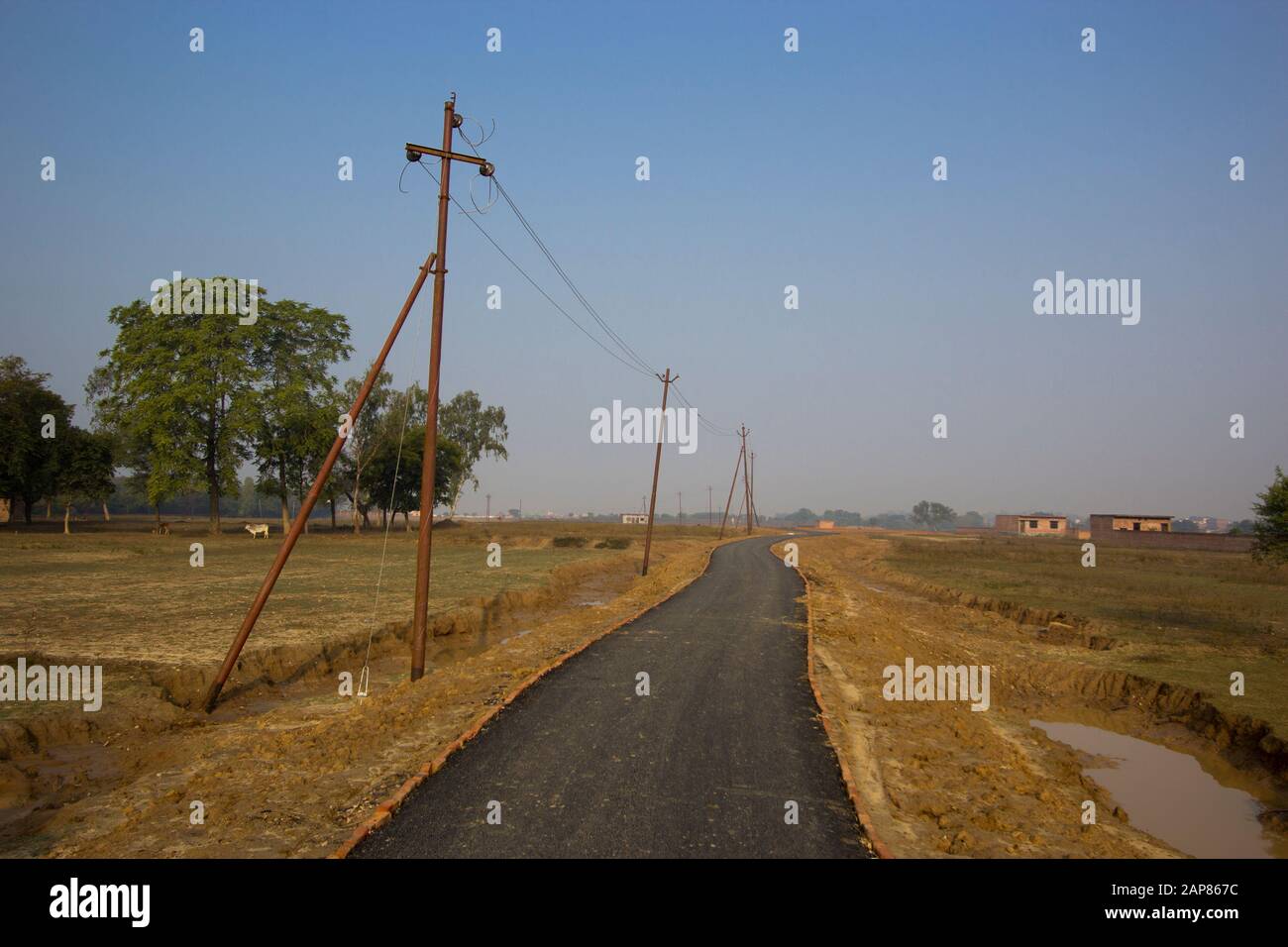 Ein Blick auf eine einspurige, gepflasterte Landstraße mit einer Reihe bescheidener, rostiger Pole für Stromleitungen. In Allalabad, Uttar Pradesh, Indien. Stockfoto