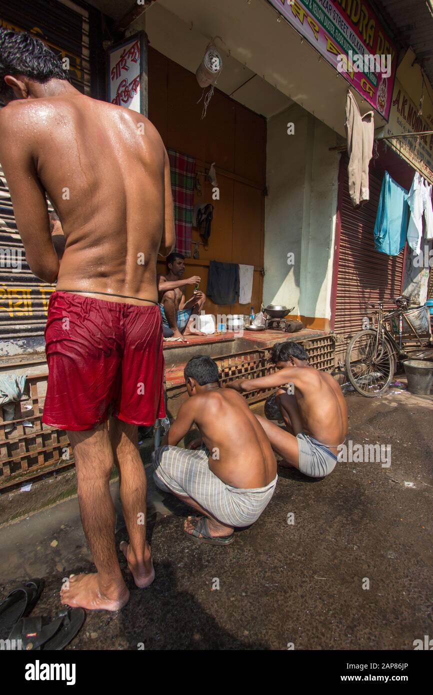 Männer und Jungen sind mit dem Baden und Reinigen auf der Straße beschäftigt. Wasserleitungen sind für Waschbedarf eingeschaltet. In Kalkutta (Kalkutta), Indien. Stockfoto