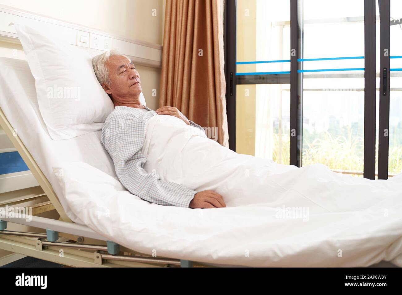 Älterer asiatischer männlicher Patient liegt im Bett und schläft in der Krankenstation oder in der betreuten Wohneinrichtung Stockfoto