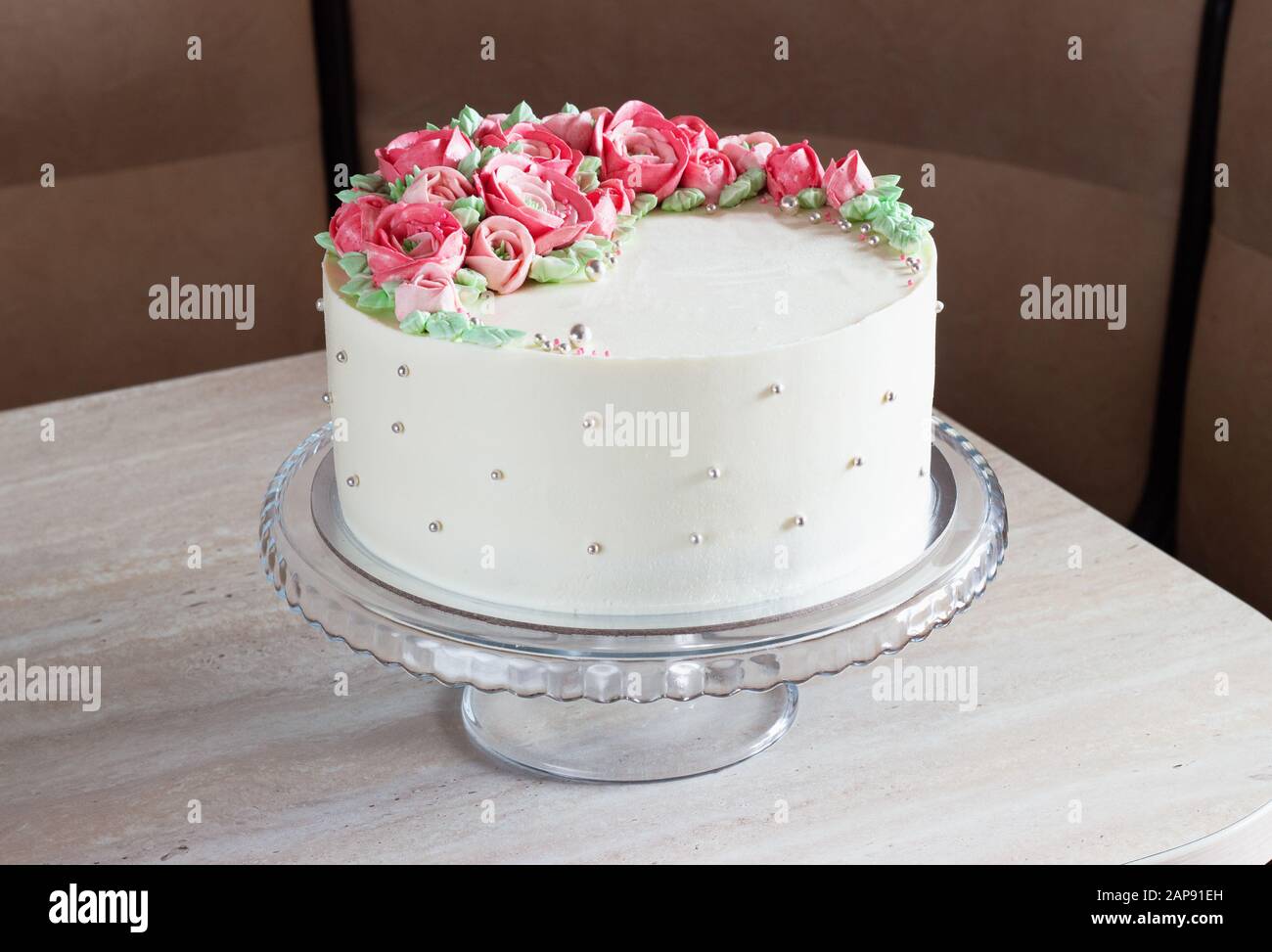 Weißer runder Kuchen mit cremefarbenen Blumen auf dem Tisch Stockfoto