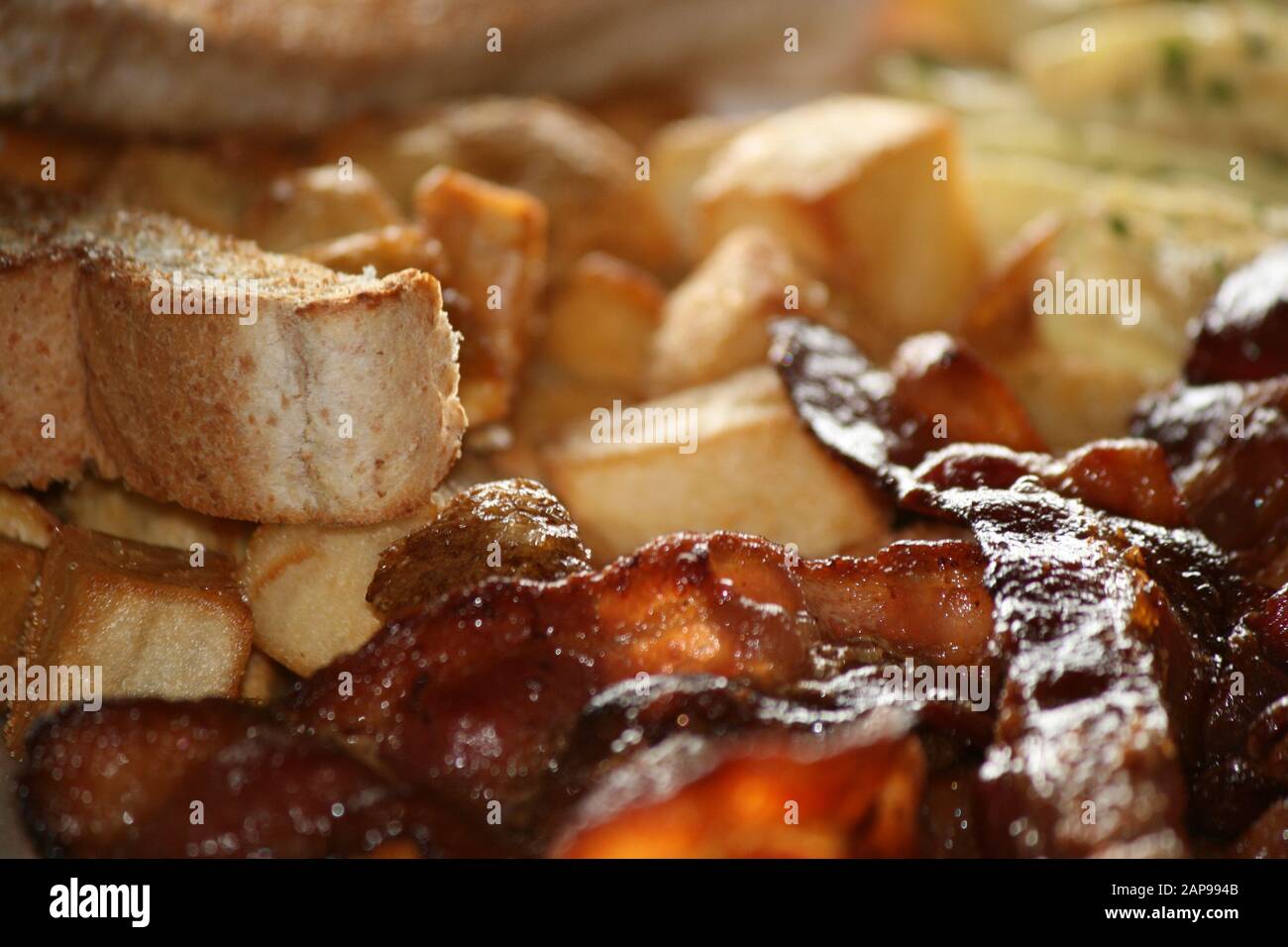 Knusprige, gut gekochte Speckstreifen aus Schweinefleisch, gebraten oder gegrillt mit Kartoffelrösti und Toast mit Tomaten auf dem Teller in Nahaufnahme zum Frühstück zum Mittag- oder Abendessen Stockfoto