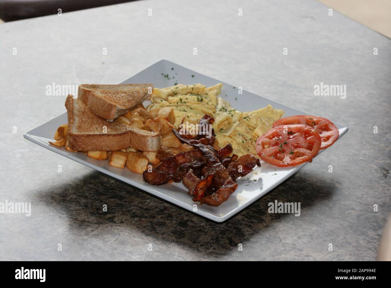 Knusprige, gut gekochte Speckstreifen aus Schweinefleisch, gebraten oder gegrillt mit Kartoffelrösti und Toast mit Tomaten auf dem Teller in Nahaufnahme zum Frühstück zum Mittag- oder Abendessen Stockfoto