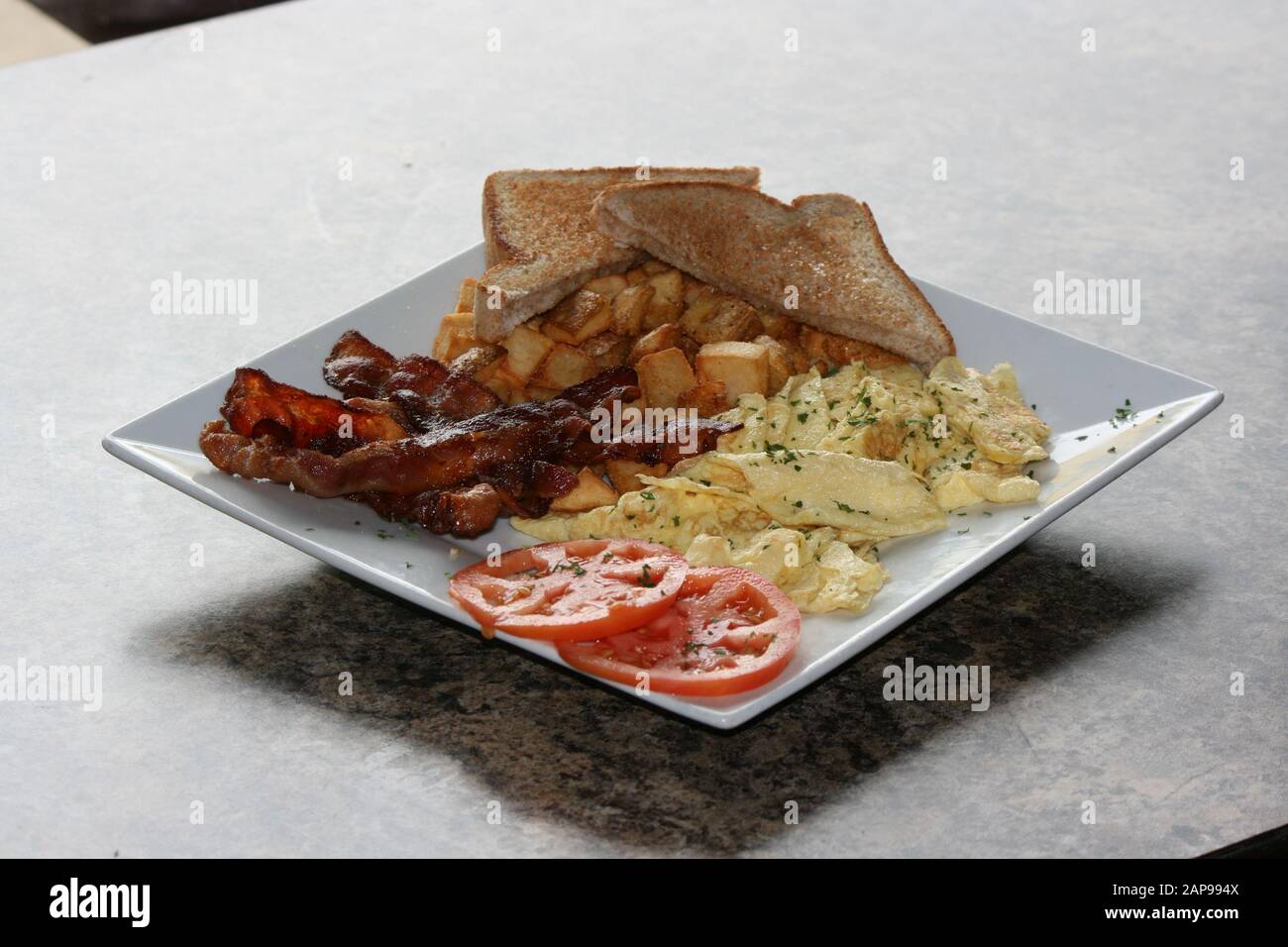 Knusprige, gut gekochte Speckstreifen aus Schweinefleisch, gebraten oder gegrillt mit Kartoffelrösti und Toast mit Tomaten auf dem Teller in Nahaufnahme zum Frühstück zum Mittag- oder Abendessen Stockfoto