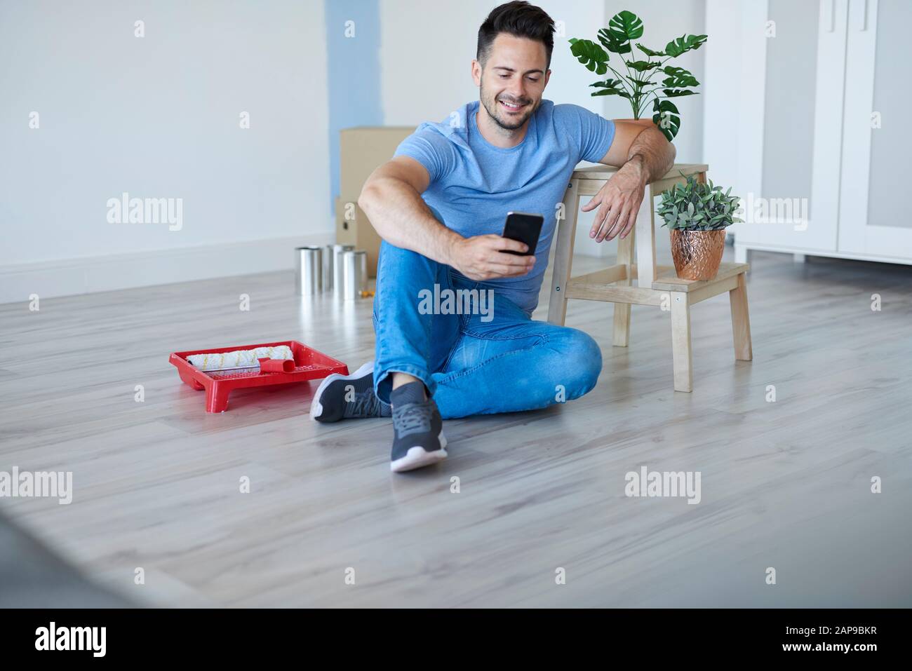 Lächelnder, junger Mann bei der Renovierung seines Hauses mit Handy Stockfoto