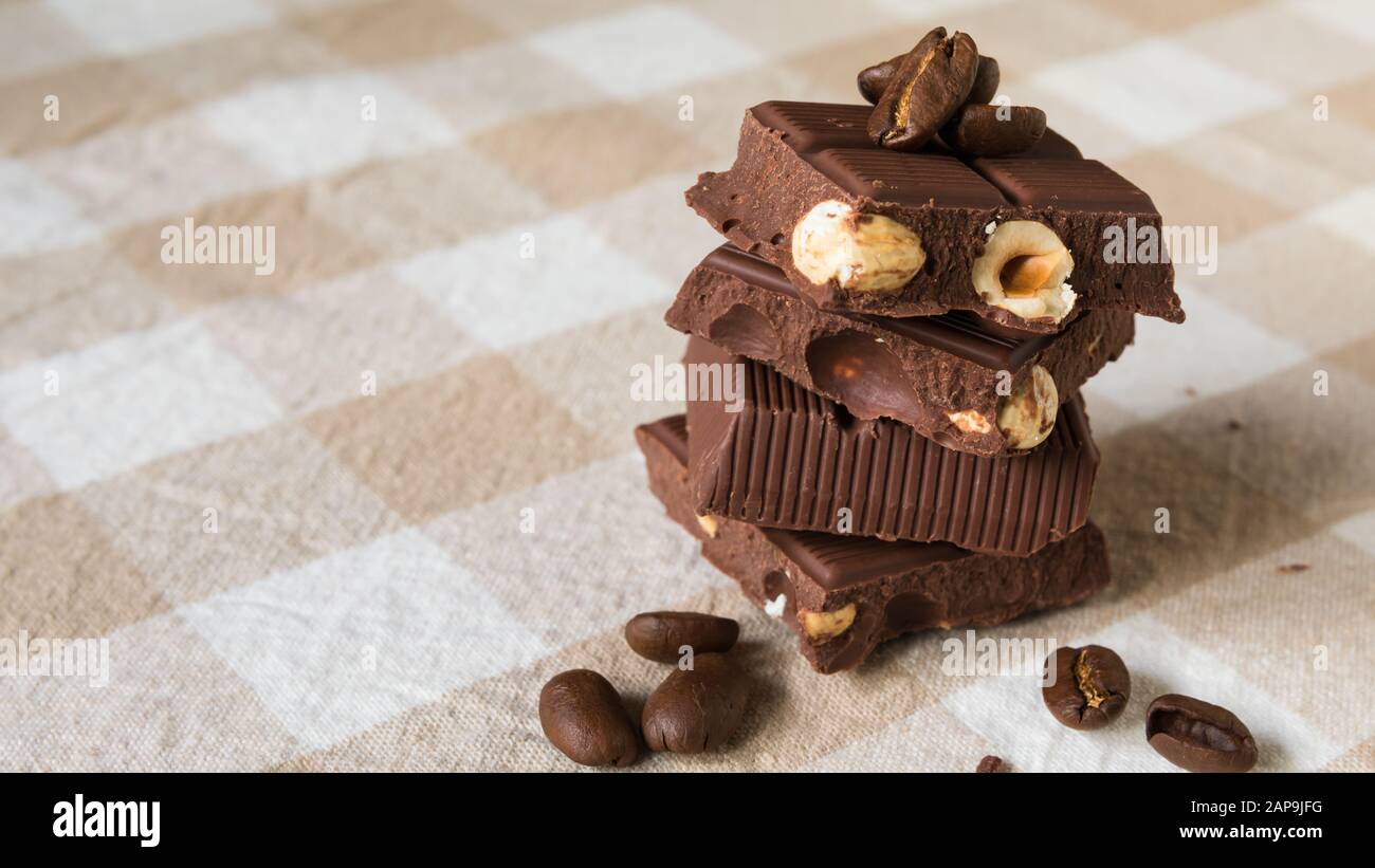 Stücke Schokolade mit Haselnüssen und Kaffeebohnen auf einem braunen Tischdecke Stockfoto
