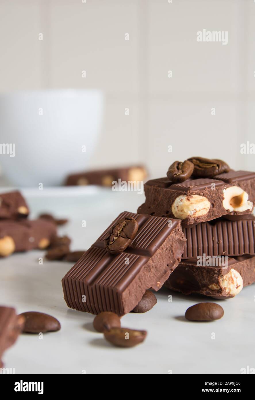 Stücke Schokolade mit Haselnüssen und Kaffeebohnen auf einem Marmortisch Stockfoto