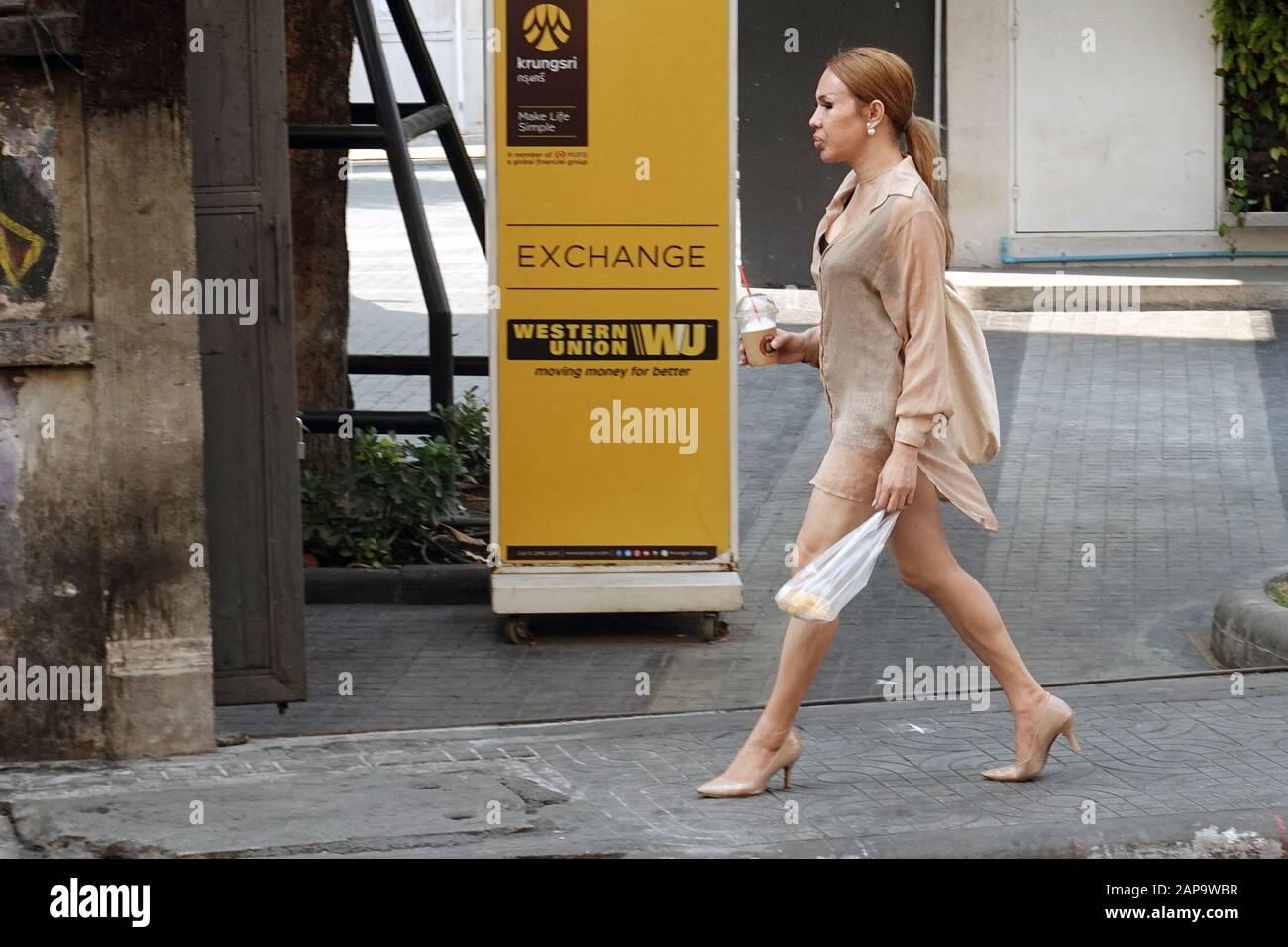 Bangkok, Thailand - 26. Dezember 2019: Transgender-Frau, Marienkind, die auf dem Bürgersteig spazieren geht und an Western Union Anzeige vorbeigeht, wo Text "Austausch" steht. Stockfoto