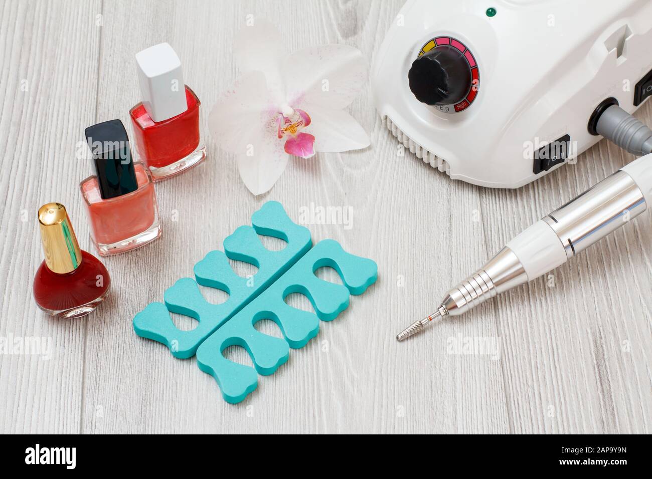 Fräser, Nagelpoliere und Zehenabscheider auf grauem Holzhintergrund. Eine Reihe von kosmetischen Tools für professionelle Hardwaremaniküre. Draufsicht. Stockfoto