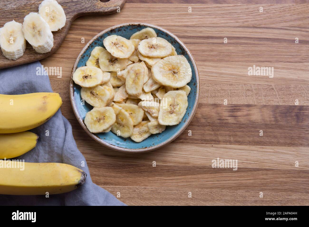 Dehydrierte, frische und getrocknete Bananenchips in der Schüssel auf dem Schneidebrett. Ansicht von oben. Stockfoto