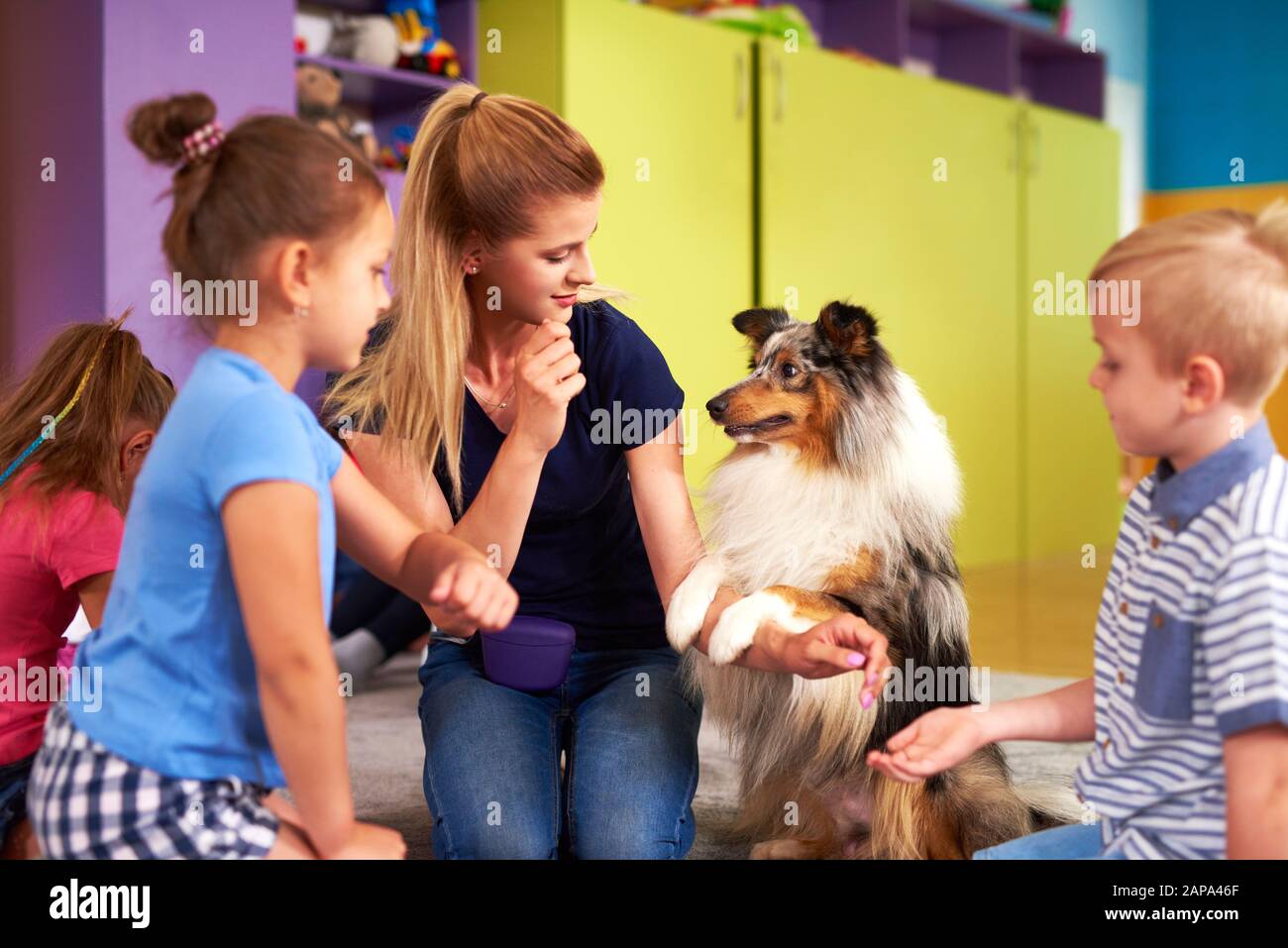Junge Frau und ihr Hund spielen mit Kindern während der Therapie Stockfoto