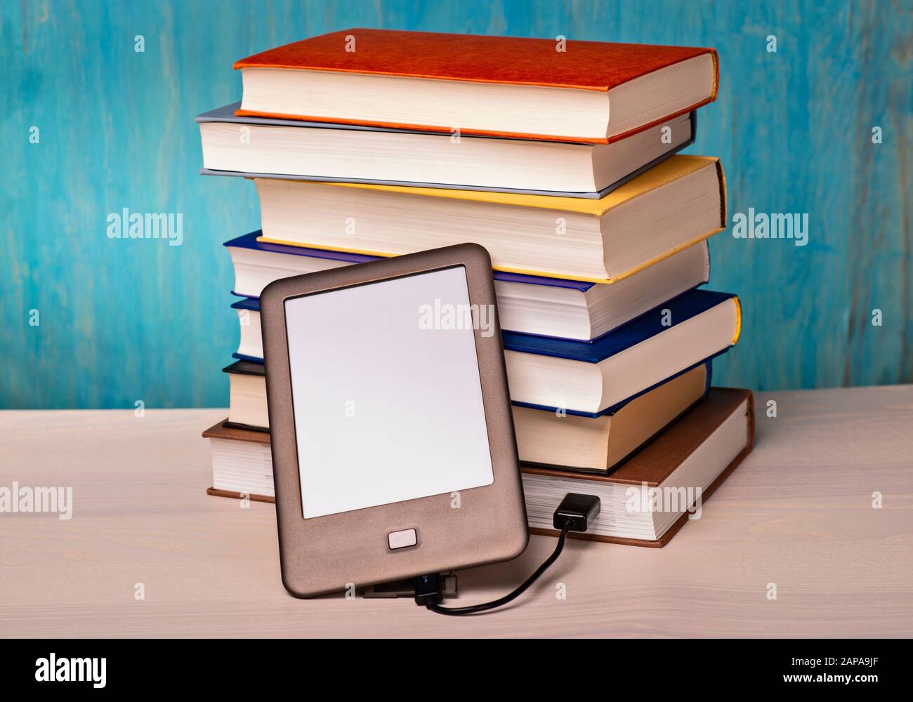 Ein E-Book-Reader ist über ein USB-Kabel mit einem Stapel von Büchern verbunden Stockfoto