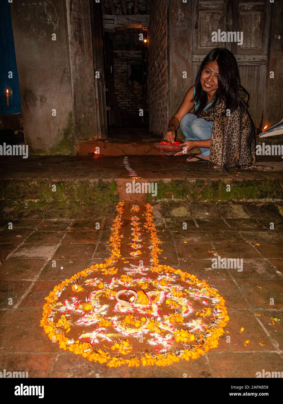 Eine Frau schafft auf dem Boden beim Festival Tihar einen Rangoli mit farbigem Reis, trockenem Mehl und Blumenblättern Stockfoto