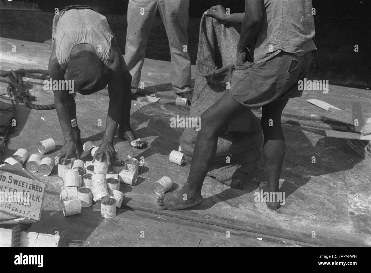 Fotos mit dem Artikel Farywell in der Zeitschrift Brothers Description: Dosen süßer Kondensmilch aus Holland werden vom Kai abgeholt und in einen Jutesack gesteckt Datum: Juli 1947 Ort: Indonesien, Niederländische Ostindien Stockfoto