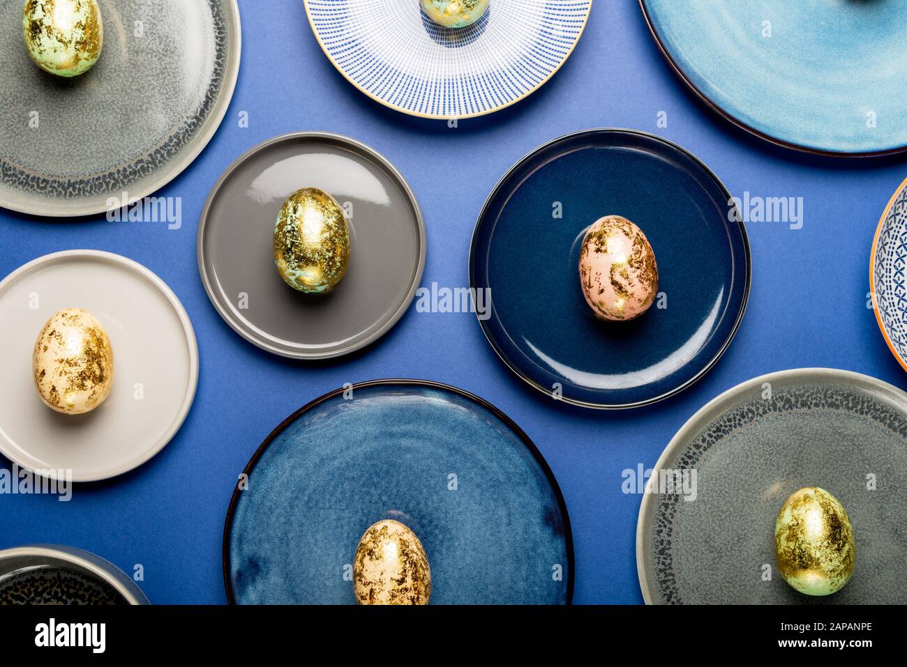 Andere keramische Platten mit goldenen Gesprenkelte Ostereier von Pastellfarben auf blauem Hintergrund. Frohe Ostern Karte Konzept, minimalistisches Design, Ansicht von oben Stockfoto