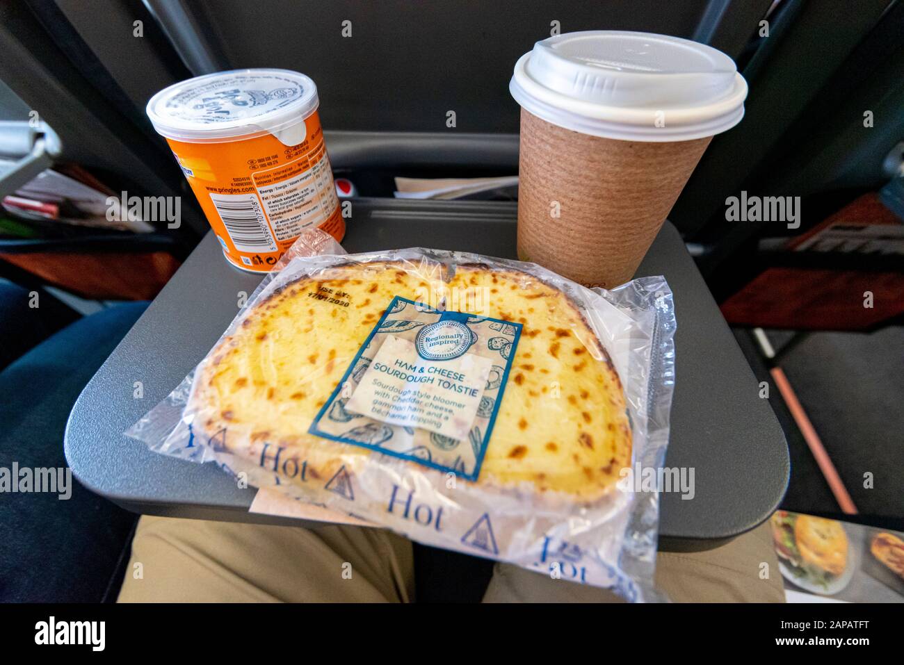 Essen und Trinken auf einem Tablett in einem easyJet Airbus A320 NEO Jet Flugzeug. Toastie mit Schinken und Käse, Pringles-Chips und Kaffee auf dem Flug Stockfoto