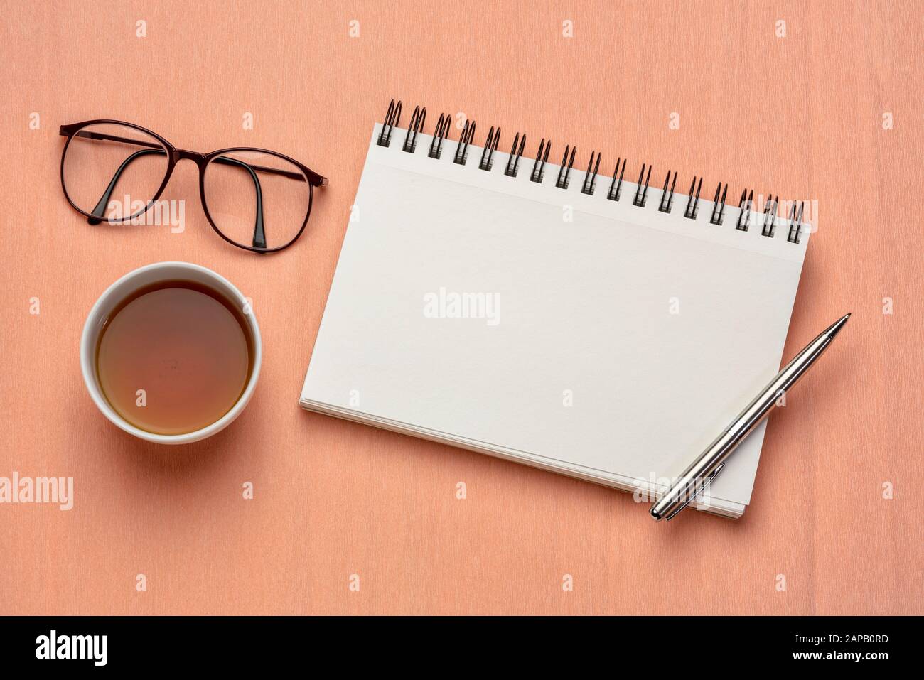 Arbeitsfläche flach mit leerem Spiralnotizbuch, Stift, Tee und Lesebrille gegen strukturiertes Papier Stockfoto